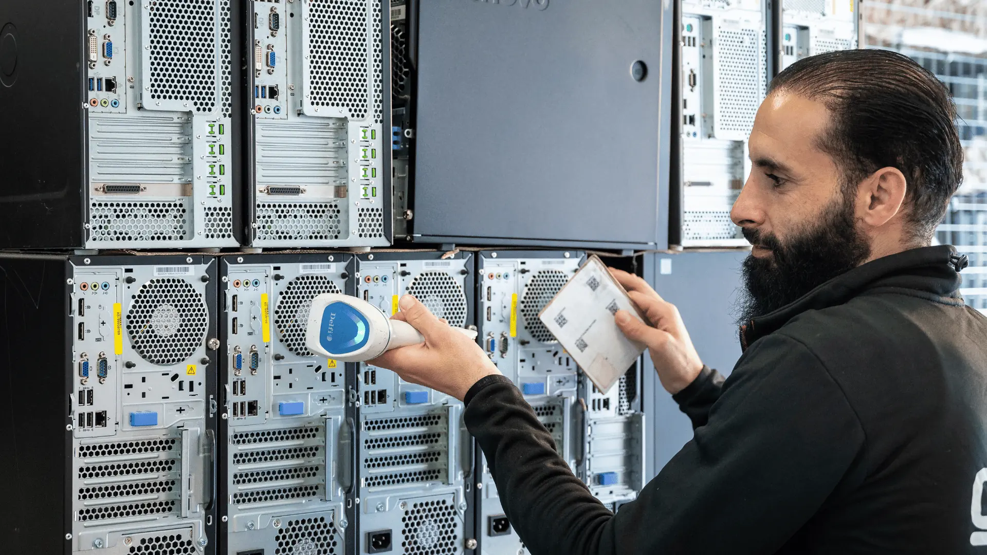 An operator scanning asset labels on a stack of desktop machines before processing