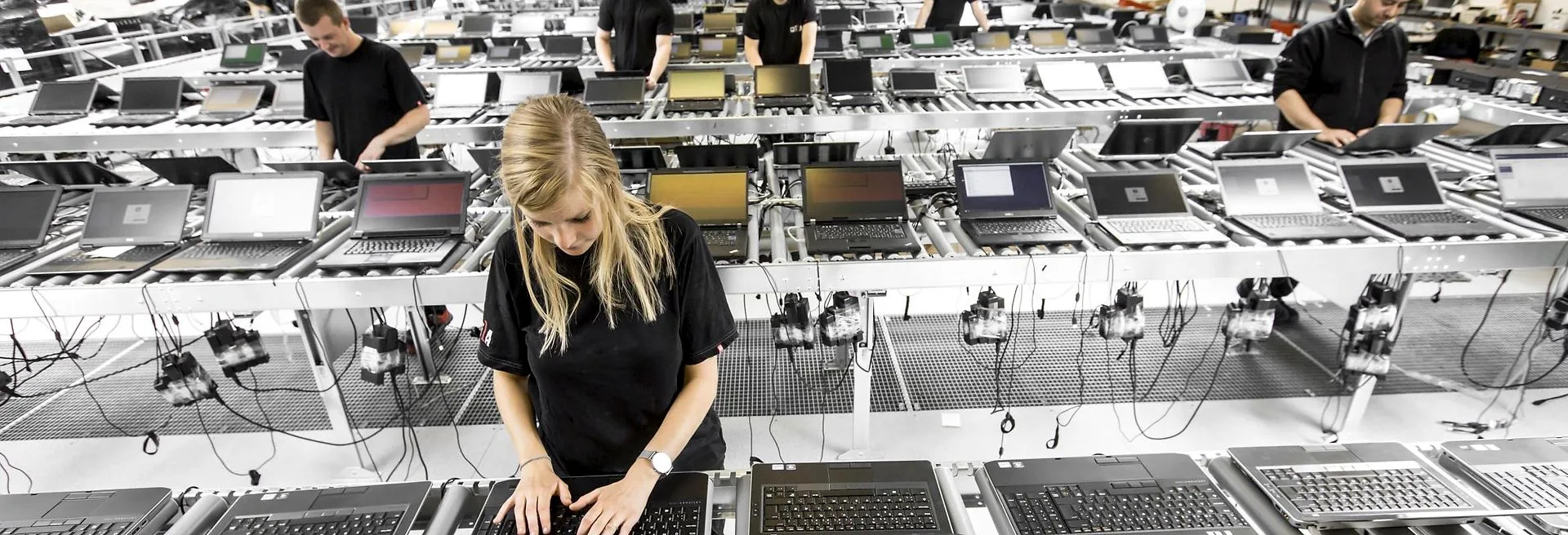 Rows of notebooks racked on shelving along the line, powered and running, with operators working the aisle