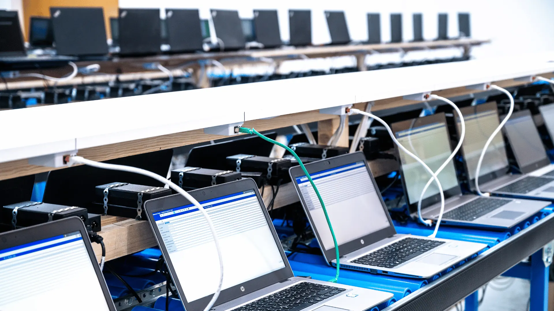 Dozens of notebooks on a refurbishment conveyor, each connected to power and network, running Wipe-Global on screen